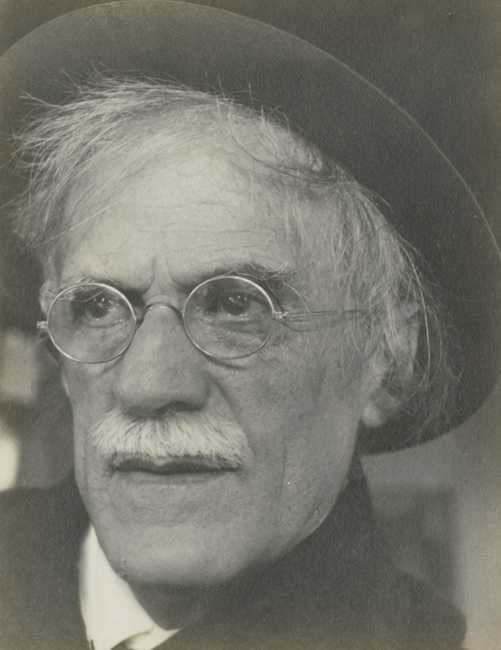[close-up in hat and glasses, mustache prominent, looking slightly to left]